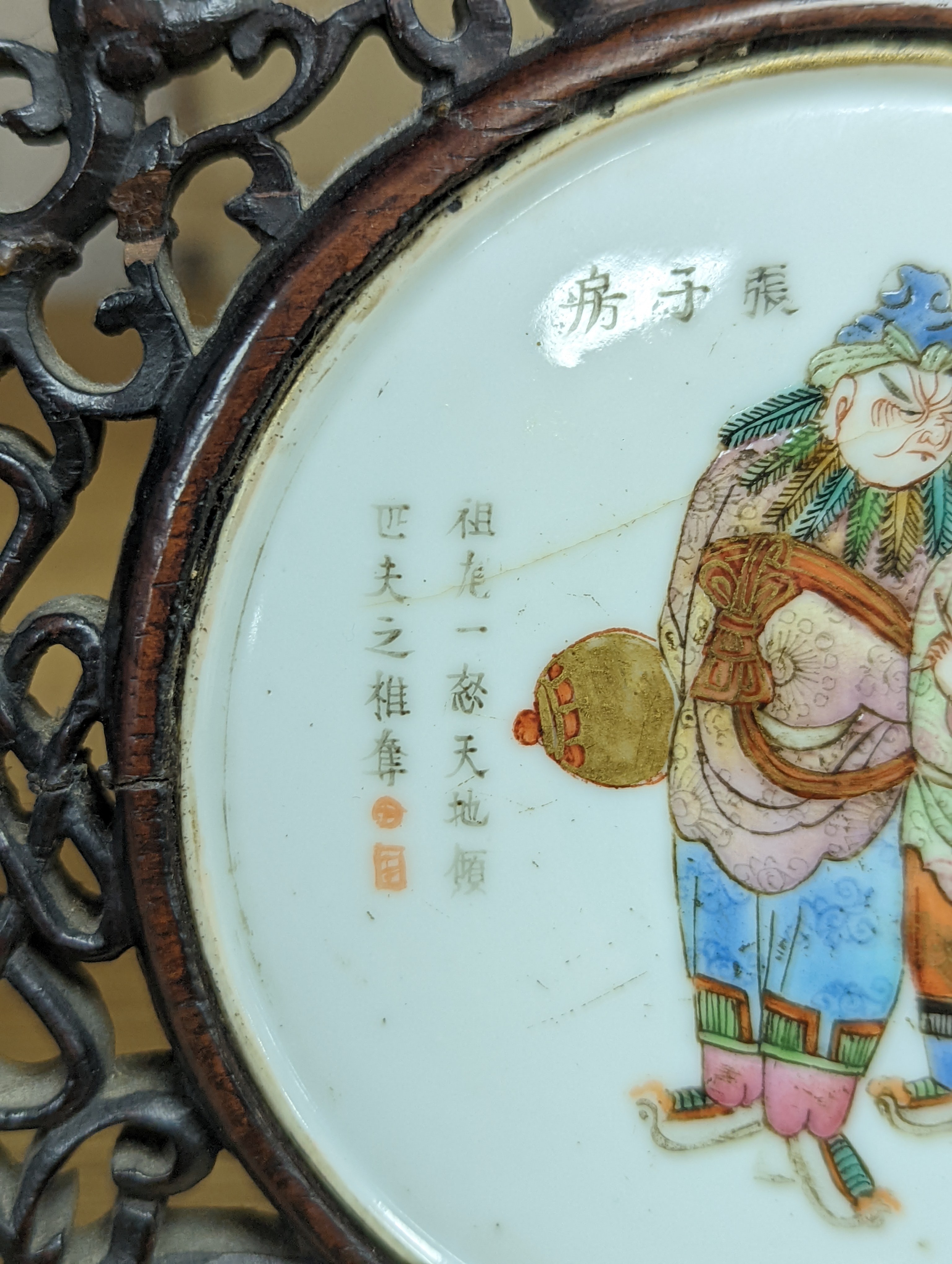 A 19th century Chinese famille rose circular plaque or cover, inset into a wood surround, cracks 15cm sq